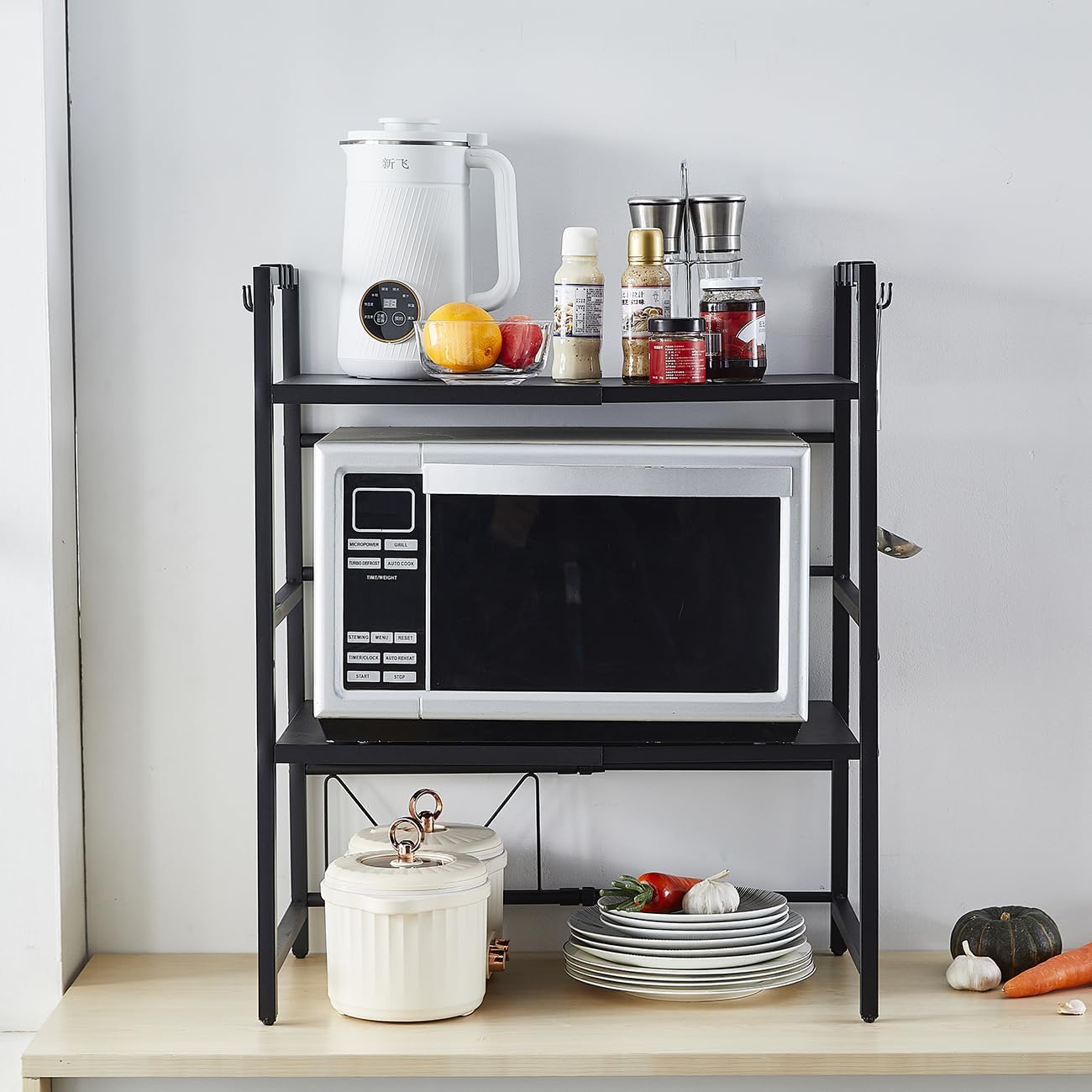 Black kitchen shelf with a microwave, plates, and various items against a light gray wall.